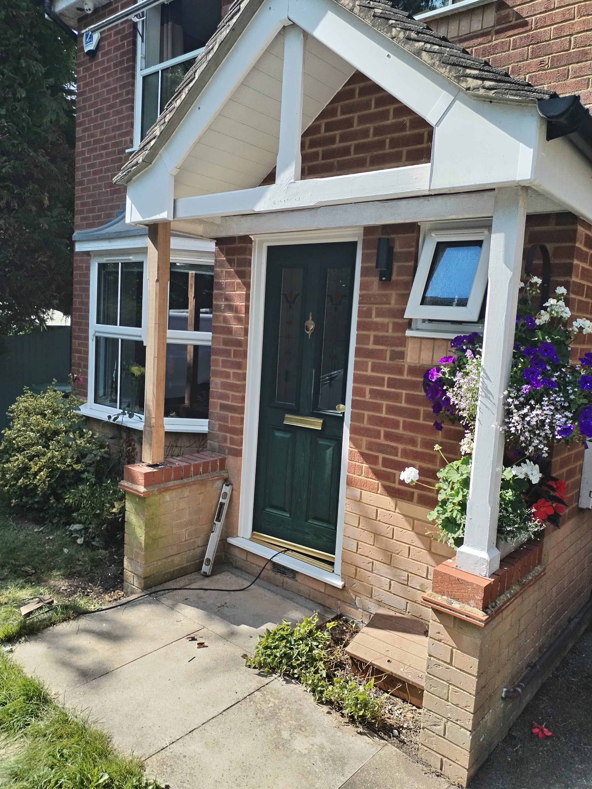 A finished gabled porch over a green front door, with hanging flower baskets