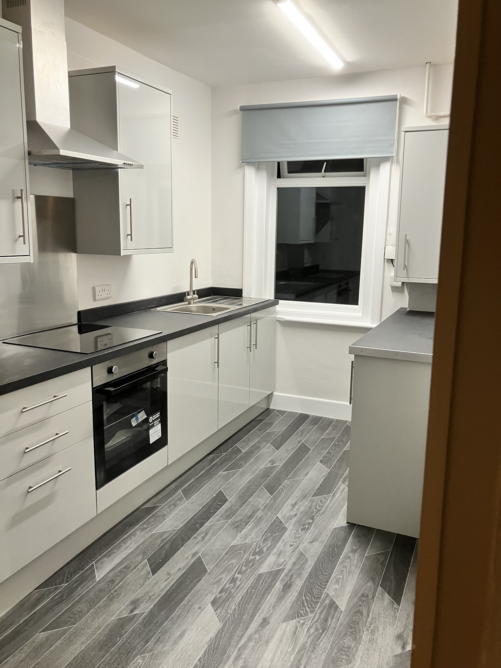 A finished galley kitchen with white gloss units, a black worktop and grey wood-effect flooring
