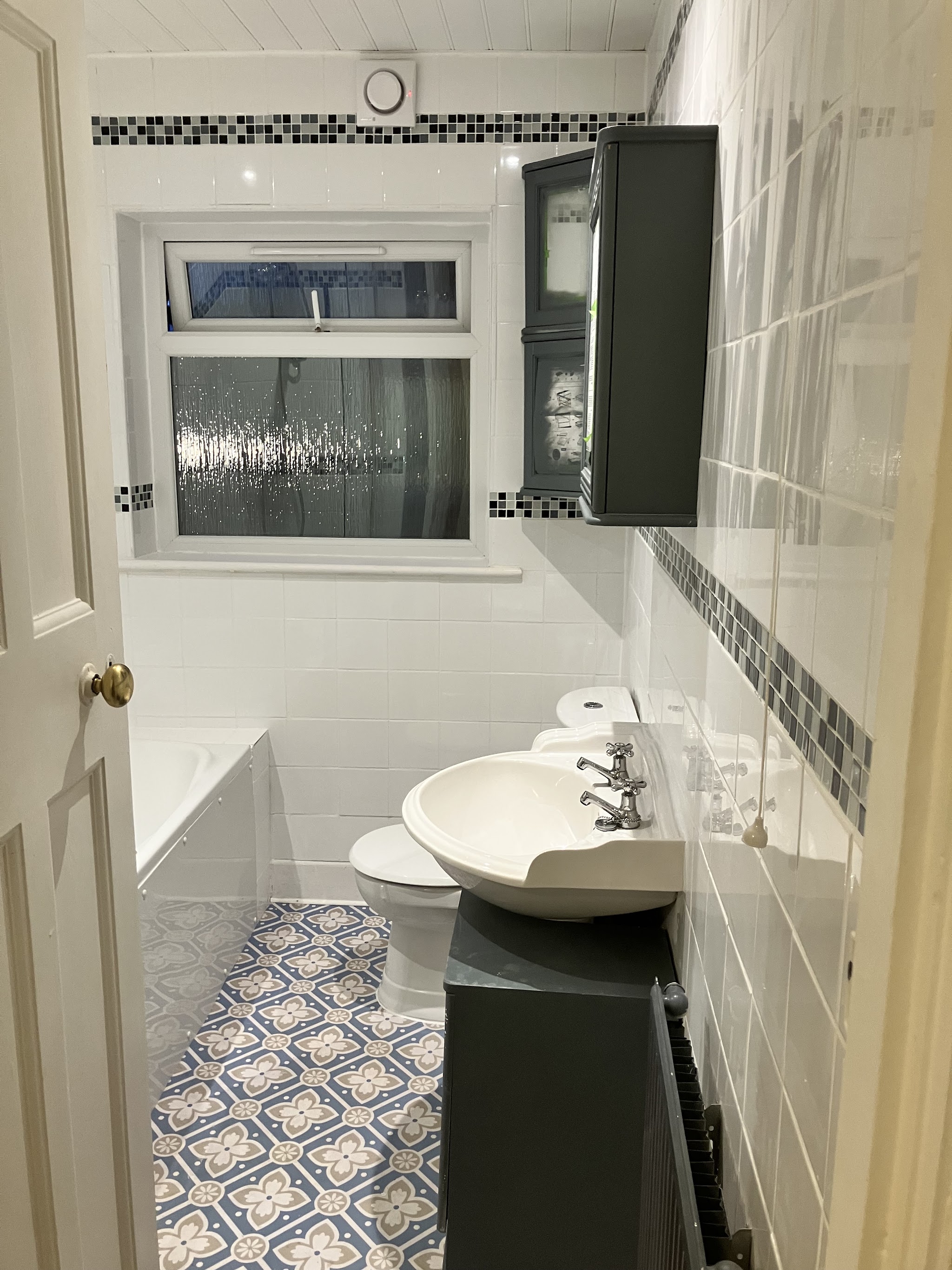 A renovated bathroom with white tiles, a mosaic border and patterned blue floor tiles