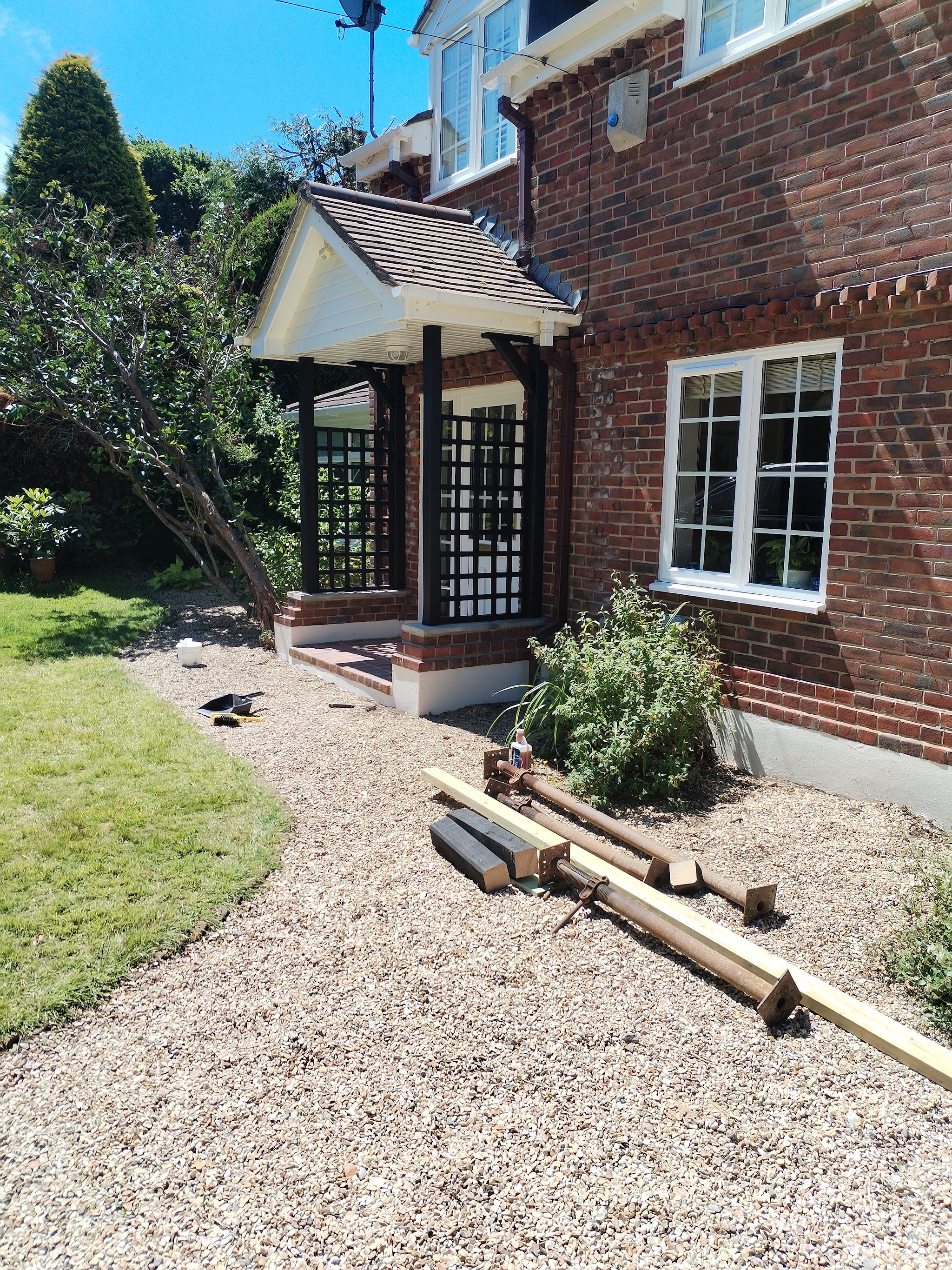 A porch build seen from the garden, with trellis posts and timber laid out on the gravel