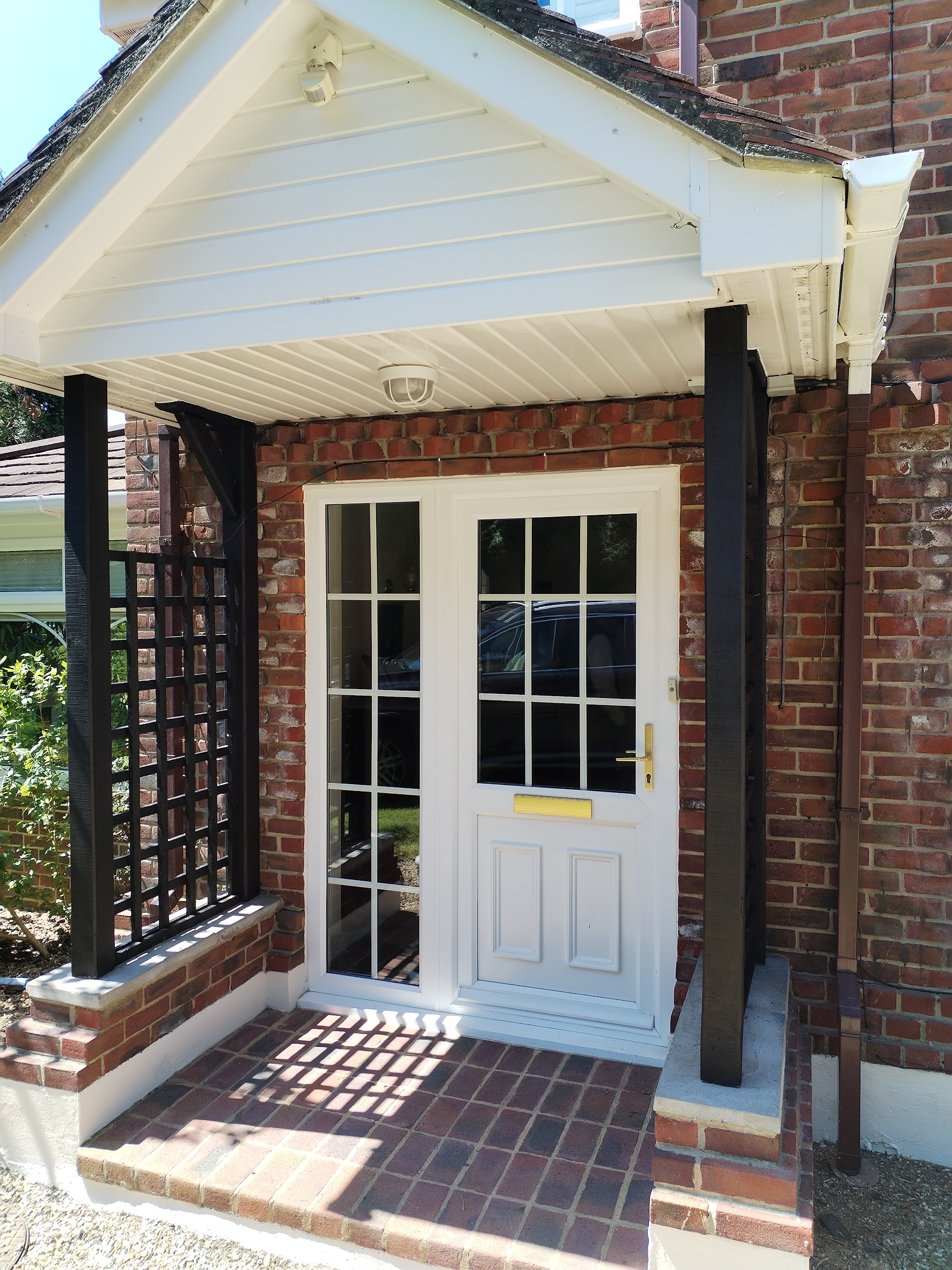 A finished front porch: white boarded gable, black trellis posts and a tiled step on a red-brick house