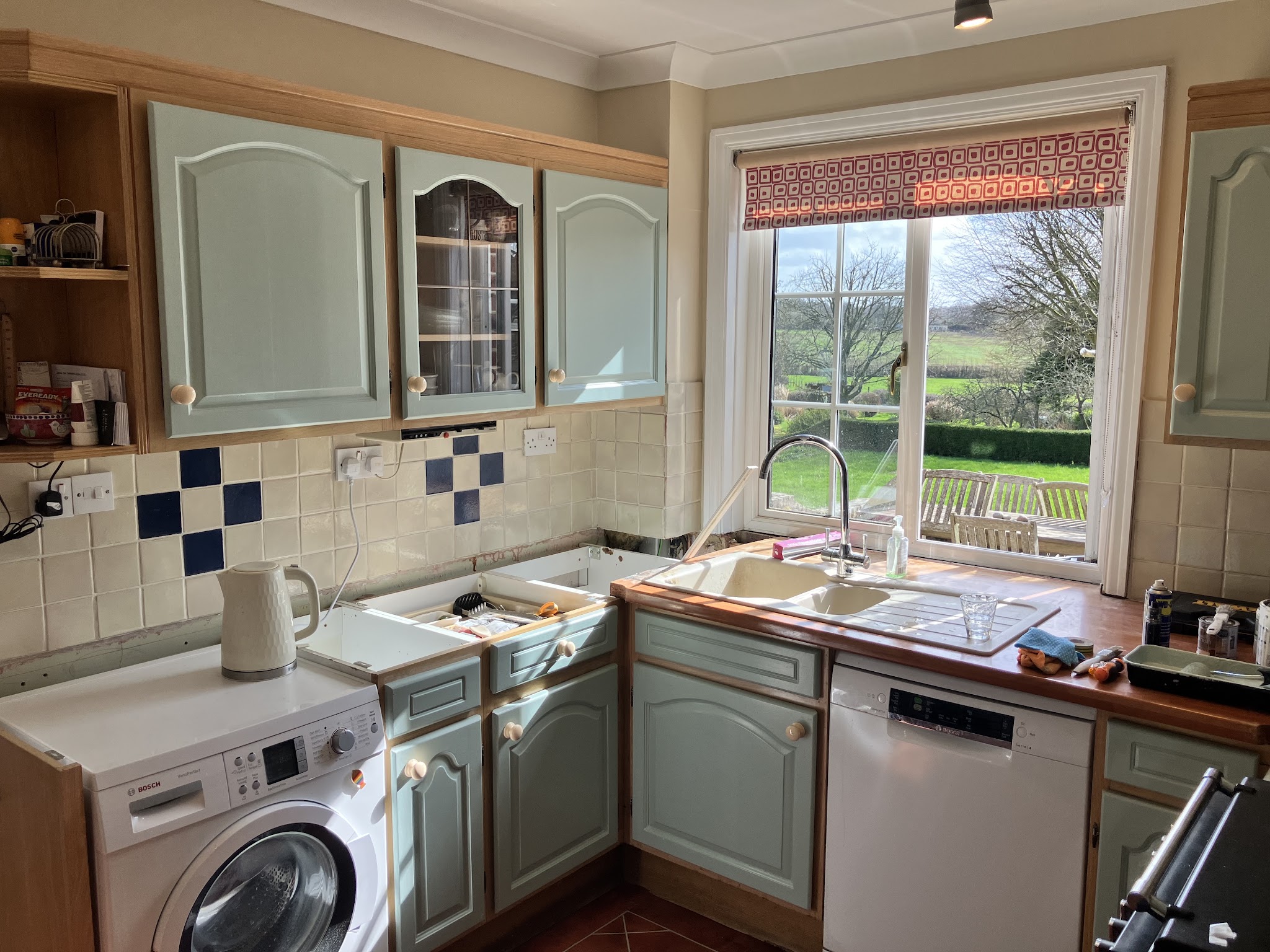 A sage-green kitchen with blue and white tile accents and a window looking out over the garden